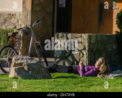 Ein Radfahrer der Frau liegt auf dem grünen Rasen, ruhen, mit ihrem Fahrrad neben ihr, im späten Nachmittag Licht in Ojai, Kalifornien. Stockfoto