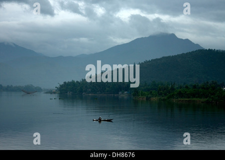 Fischer in seinem Kanu vor Sonnenaufgang, Vietnam mit Seen & Bergen umgeben. Stockfoto