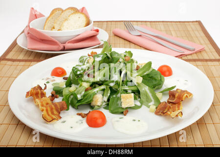 Feldsalat mit Kartoffeldressing, Brot Croutons, gebratenem Speck und Stangenbrot Stockfoto