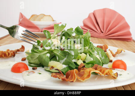 Feldsalat mit Kartoffeldressing, Brot Croutons, gebratenem Speck und Stangenbrot Stockfoto