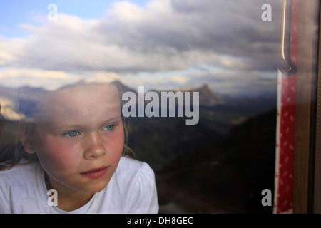 Verträumte Mädchen starrte durch Fenster mit Reflexion der Berge und Wolken, Dolomiten, Italien Stockfoto