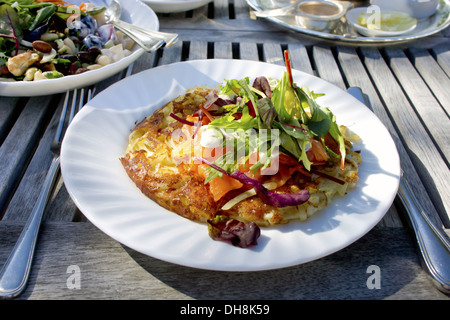 : Kartoffel Rösti auf eine Platte mit geräuchertem Lachs und Salat auf einem Holztisch in einem Garten. Stockfoto
