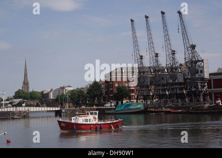 Vier Kräne neben Bristol Stadt-Docks mit einem kleinen Boot den Hafen überqueren Stockfoto