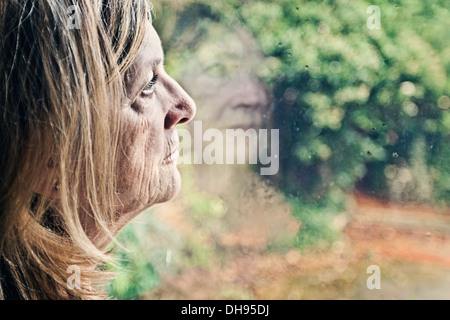 Senior Lady Blick aus Fenster Stockfoto