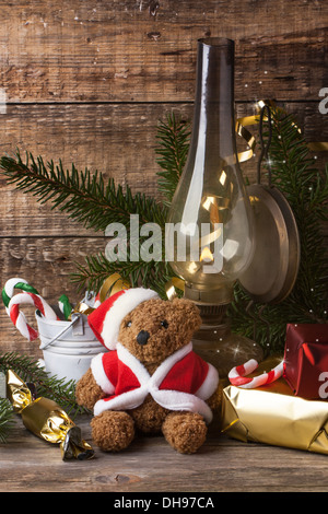 Weihnachts-Dekoration mit antiken Teddybär in Nikolausmütze mit brennenden Vintage Lampe über hölzerne Hintergrund Stockfoto