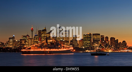 Australien Sydney CBD Panorama Blick bei Sonnenuntergang mit beleuchteten Wolkenkratzern und Marine Schiff mitten im Hafen mit Lichtern Stockfoto