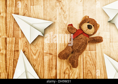 Niedlicher Bär Spielzeug auf laminierten Holzboden mit Origami Papierflieger Stockfoto