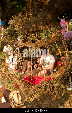 Festivalbesucher beim Secret Garden Music Festival sitzen in einem riesigen Weidenkorb zusammen rollenden Rauchen Material in der Sonne. Stockfoto