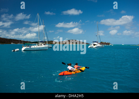 Zwei Personen paddeln vorbei an großen weißen Segelbooten im karibischen Meer in den British Virgin Islands an einem funkelnden Sommertag Stockfoto