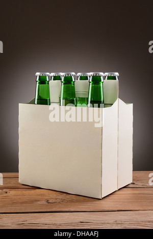 Nahaufnahme von einem six-Pack von grünen Bierflaschen auf einem rustikalen Holztisch. Hochformat mit einer leichten bis dunkelgrauen Hintergrund vor Ort. Stockfoto