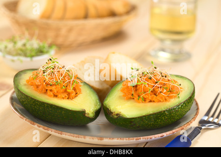 Avocado-Hälften gefüllt mit geriebenen Karotten und bestreut mit Alfalfasprossen auf Platte serviert mit Baguette Scheiben Stockfoto