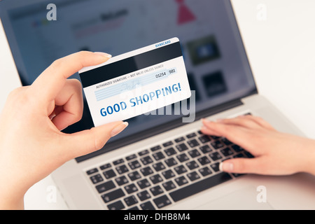 Zarte Frauenhand hielt eine Bankkarte über einen Laptop. Auf der Karte ist "Gute shopping" geschrieben. Sie können jede Inschrift auf der Karte setzen. Stockfoto
