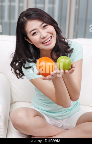 Junge Frau sitzt auf der Couch, mit Apfel und orange Stockfoto