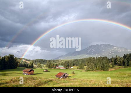 bunte Regenbogen über Almwiesen mit Holzhütten, Bayern, Deutschland Stockfoto