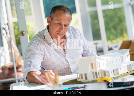 Eine Landhausküche. Ein Modell eines Hauses auf dem Tisch. Ein Haus zu entwerfen. Ein Mann mit einem Bleistift auf einem Plan zeichnen. Stockfoto