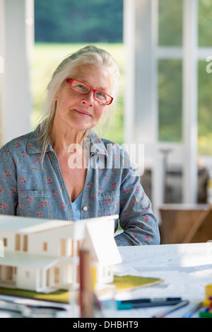 Eine Landhausküche. Ein Modell eines Hauses auf dem Tisch. Ein Haus zu entwerfen. Eine Frau hält einen Stift. Stockfoto
