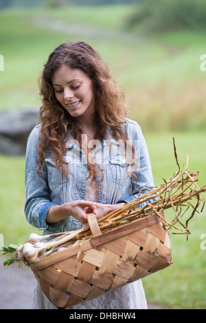 Eine junge Frau trägt einen Korb mit frisch geernteten Knoblauch und Gemüse. Stockfoto