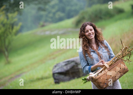 Eine junge Frau trägt einen Korb mit frisch geernteten Knoblauch und Gemüse. Stockfoto