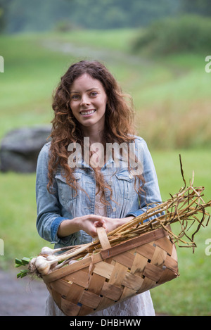 Eine junge Frau trägt einen Korb mit frisch geernteten Knoblauch und Gemüse. Stockfoto