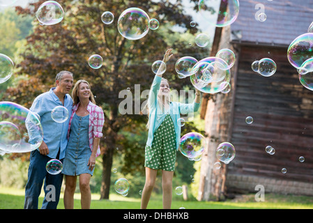 Eine Familie sitzen auf dem Rasen vor einer Bar, Seifenblasen und lachen. Stockfoto