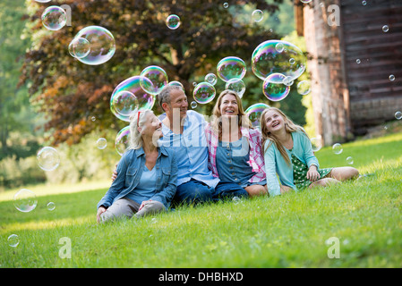 Eine Familie sitzen auf dem Rasen vor einer Bar, Seifenblasen und lachen. Stockfoto