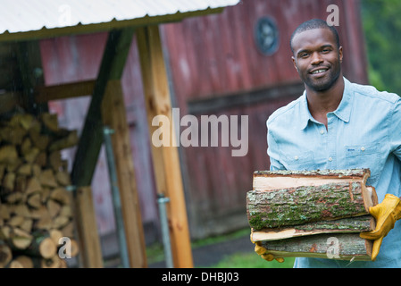 Ein junger Mann mit einem Haufen der Protokolle in der Logstore. Leben auf dem Bauernhof. Stockfoto