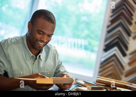 Ein junger Mann an seiner Werkbank in einem Bild Framing Studio. Umgeben von Proben. Stockfoto