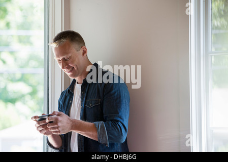 Ein Mann steht in einer ruhigen Ecke ein Café, ein smart Phone verwenden. Stockfoto