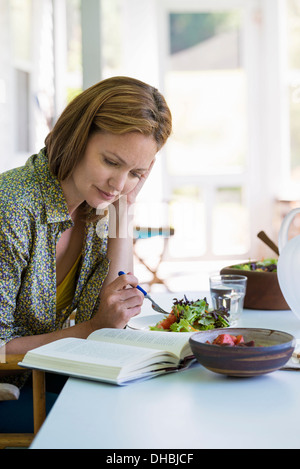 Eine Frau sitzt an einem Tisch, ein Buch zu lesen. Stockfoto