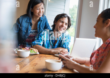 Eine Gruppe von drei Personen in einem Café. Gemeinsame Nutzung eines Laptops und Smartphones verwenden. Stockfoto