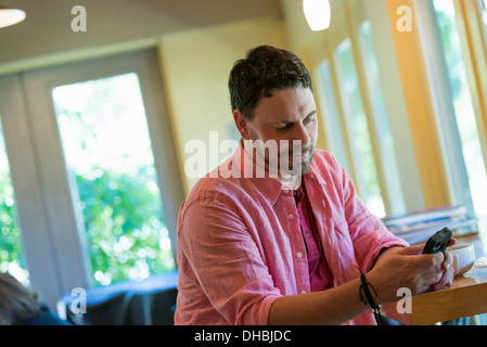 Ein Mann sitzt in einem Cafétisch, mit einem Smartphone. Stockfoto