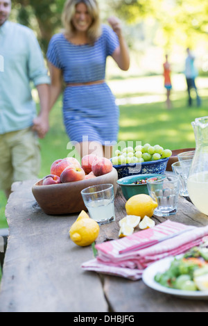 Ein Sommer-Buffet von Obst und Gemüse, auf einen Tisch gelegt. Menschen im Hintergrund. Stockfoto