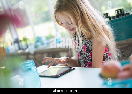 Ein junges Mädchen in einem geblümten Kleid mit einem digitalen Tablet. An einem Tisch sitzen. Stockfoto