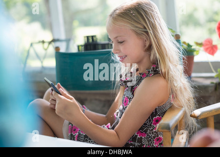 Ein junges Mädchen in einem geblümten Kleid mit einem digitalen Tablet. An einem Tisch sitzen. Stockfoto