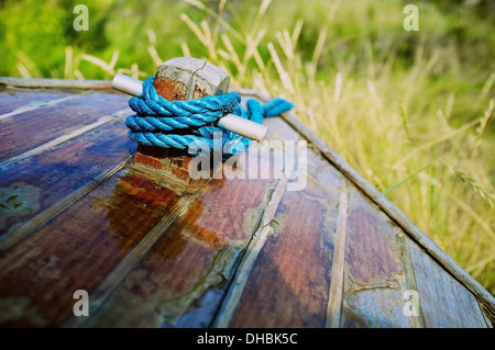 Abstraktes Bild des Bogens (vorne) der kleinen Holzboot mit blauen Seil aufgewickelt um eine kurze Nachricht mit Grass im Hintergrund. Stockfoto