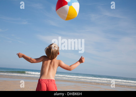 Ein Junge in der Badehose am Strand, mit einer großen Beach-Ball in der Luft über ihn. Stockfoto