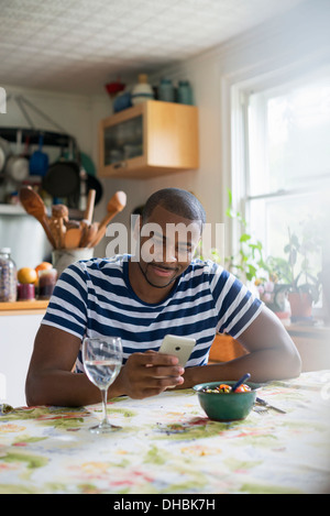 Ein Mann sitzt an einem Tisch mit einem Smartphone. Obst Dessert und ein Glas Wein zur hand. Stockfoto