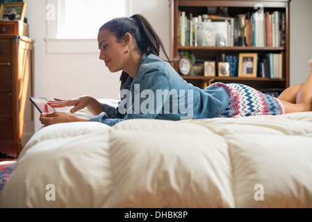 Eine junge Frau liegt auf ihrem Bett mit einem digitalen Tablet.