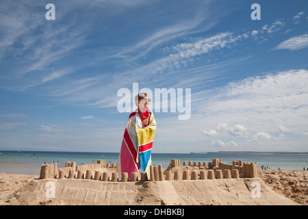 Ein Junge steht neben einer Sandburg, oben auf einem Hügel aus Sand. Strand. Stockfoto