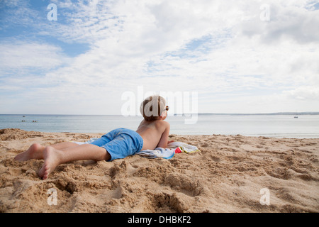 Ein Junge, der auf seiner Vorderseite auf dem Sand, Blick auf das Meer liegen. Stockfoto