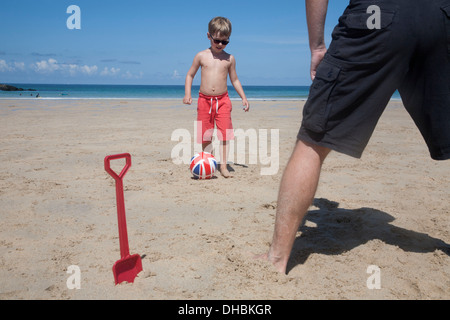 Ein Junge spielt Fußball mit einem Mann auf dem Sand. Vater und Sohn. Ein Strand Spaten aufrecht in den Sand. Stockfoto