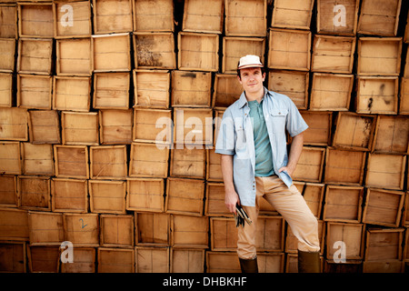 Ein Bauer steht man vor einer Wand aus gestapelten Holzkisten für Produkte. Stockfoto