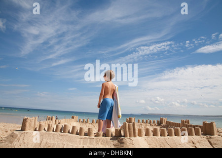 Ein Junge steht neben einer Sandburg, oben auf einem Hügel aus Sand. Strand. Stockfoto