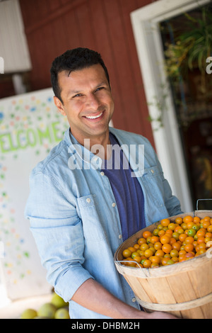 Ein Bauernhof, Anbau und Verkauf von Bio-Gemüse und Obst. Ein Mann hält eine Schale mit Korb mit frisch gepflückten Tomaten. Stockfoto