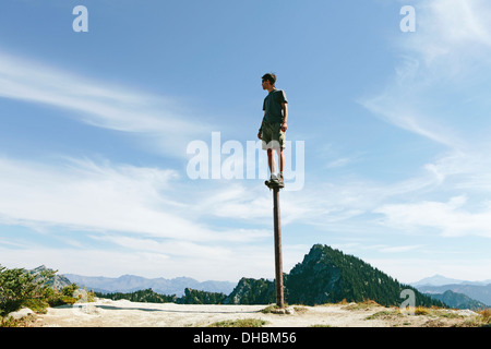 Ein Mann stehend balancieren auf Metallpfosten mit Blick auf weitläufige Himmel auf Überraschung Gebirge alpinen Seen Wildnis Mt Stockfoto