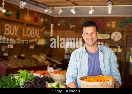 Ein Bauernhof, Anbau und Verkauf von Bio-Gemüse und Obst. Ein Mann hält eine Schale mit Korb mit frisch gepflückten Tomaten. Stockfoto