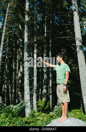 Ein kleiner Junge steht im Wald eine Smartphone ein selfy oder ein Foto im Olympic Nationalpark zu halten. Stockfoto