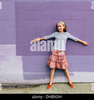 Ein zehn Jahre altes Mädchen in einen Stufenrock, stehend mit ausgebreiteten Arme an eine Wand gelehnt. Stockfoto