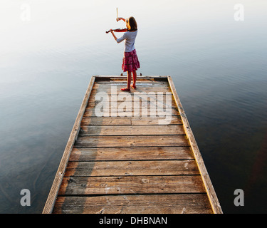 Ein zehn Jahre altes Mädchen, das Geigenspiel im Morgengrauen auf einem hölzernen Dock. Stockfoto