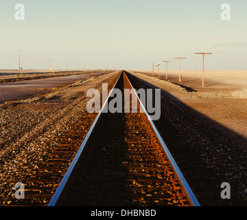 Eisenbahnschienen erstreckt sich über die flache Wüstenlandschaft von Utah in der Abenddämmerung. Stockfoto